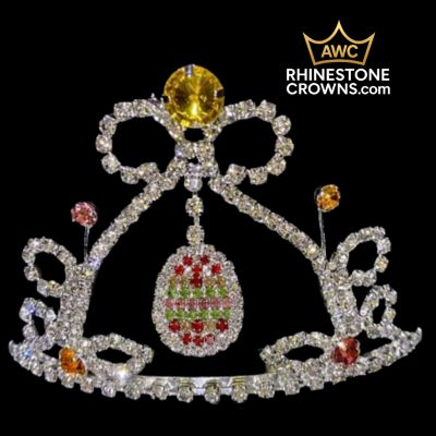 The Easter Egg Dangle Series - 3.25" Crown features a large yellow gem, a central egg-shaped pendant with red and green accents, and smaller stones. The AWC RHINESTONE CROWNS.com logo appears at the top right of the black background.