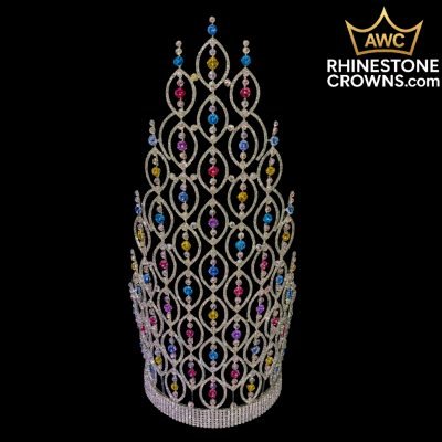 The Rainbow Belle Series - 20" Crown, a tall rhinestone crown with an ornate woven lattice design and blue, pink, and yellow gems, is shown on a black background. PRE-PURCHASE ONLY—ships up to 4 weeks after purchase. Order separately if needed sooner.