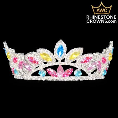The Rainbow Dominique Series 2"x4" Fully Round Crown, jeweled with pink, yellow, and blue rhinestones on silver, is ready to ship with more in production. Displayed on black background; AWC RHINESTONE CROWNS.com logo appears top right.